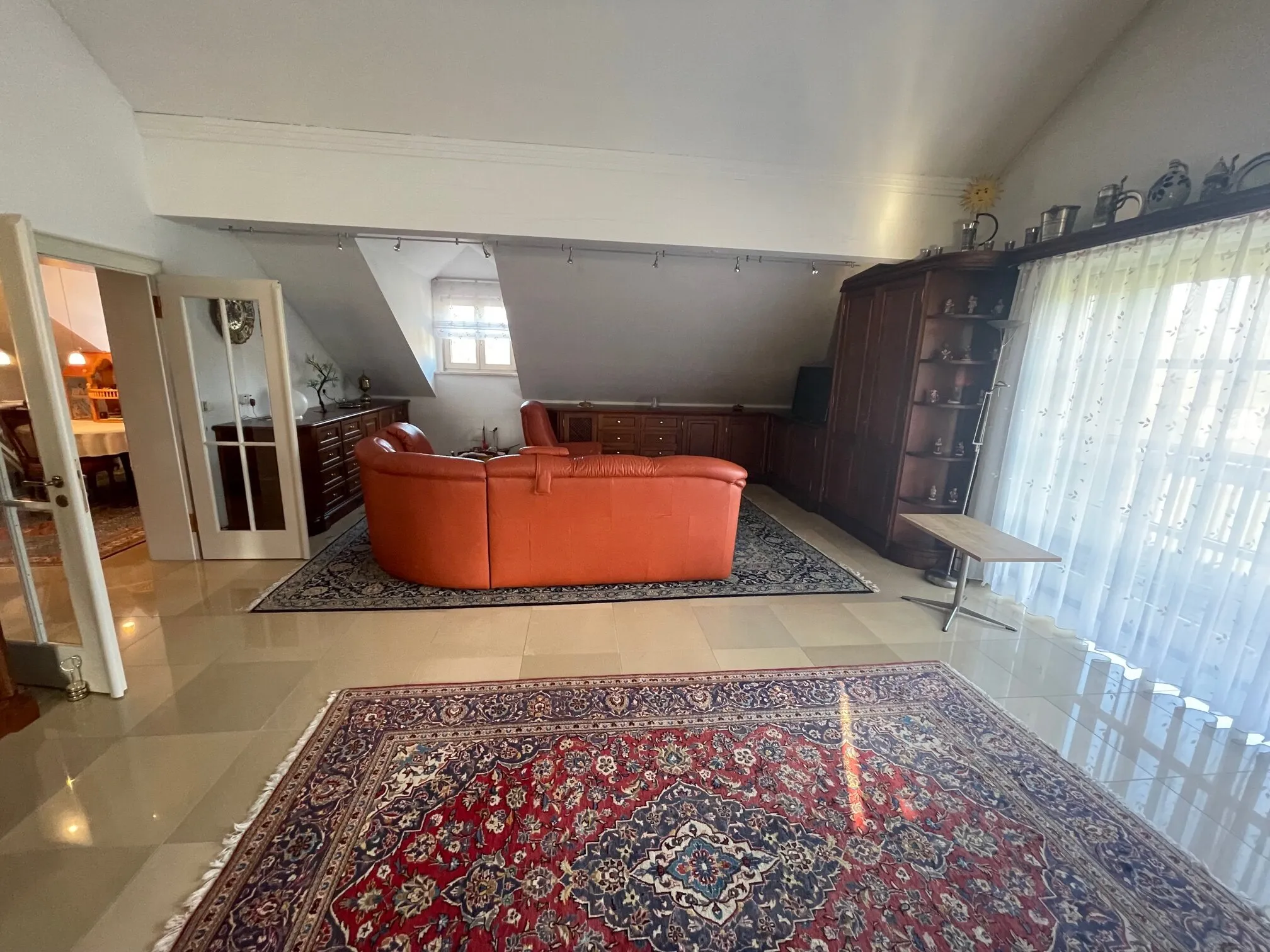 Großer Wohnbereich mit orangem Sofa und Perserteppich